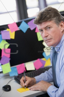 Businessman in office at monitor with notes on it writing