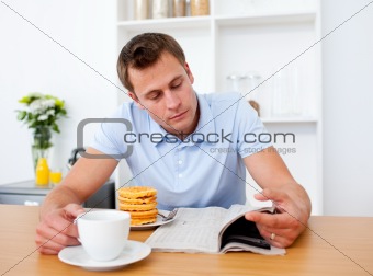 Concentrated man reading a newspaper while having breakfast 