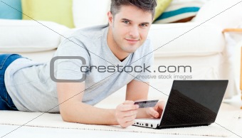 Smiling man lying on the floor with laptop holding a card
