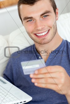 Animated young man holding a card and a latop sitting on the sofa at home