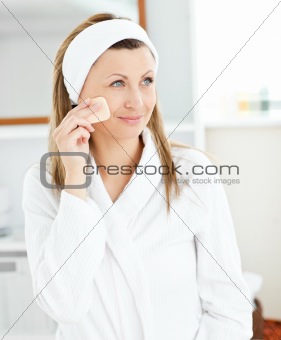 Charming young woman putting cream on her face in the bathroom