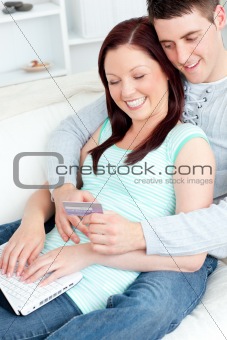 Enamored couple lying on the sofa with a laptop and a card