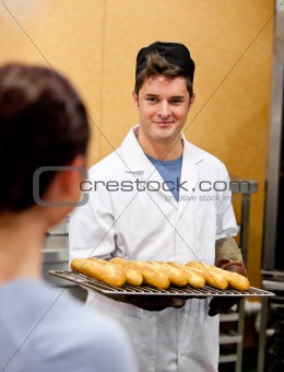 Glowing young male baker holding baguettes in the kitchen