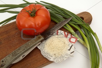 Tomato, salt on the newspaper, a knife and an onions on a board