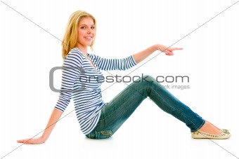 Smiling beautiful teen girl sitting on floor and pointing finger at something
