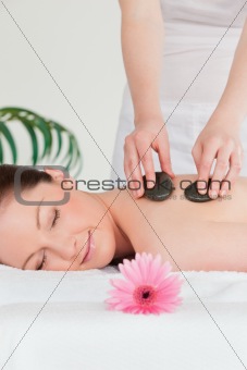 Happy young woman having a hot stone massage and a pink gerbera
