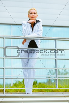 Portrait of smiling business woman leaning on railing at office building 
