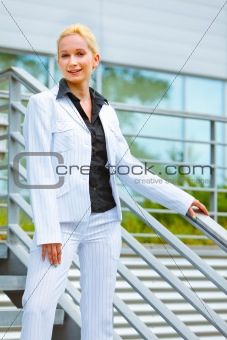 Smiling business woman standing on stairs at office building  and holding hand on railing 
