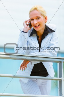 Smiling business woman leaning on railing at office building and talking on mobile
