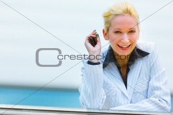 Smiling business woman with mobile in hand leaning on railing at office building

