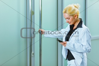 Smiling business woman with mobile entering office building 
