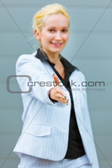 Standing at office building smiling business woman stretches out hand for handshake
