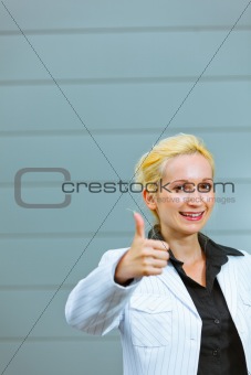 Standing at office building smiling business woman showing thumbs up gesture
