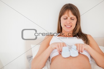 Lovely pregnant woman playing with little socks while lying on a