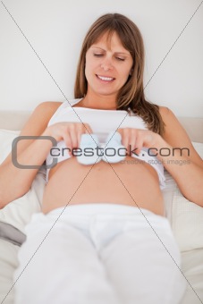 Beautiful pregnant woman playing with little socks while lying o