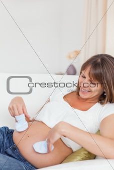 Pregnant woman playing with baby shoes while lying