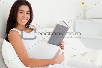 Beautiful pregnant woman reading a book while lying on a bed