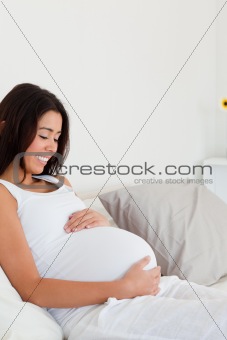 Gorgeous pregnant woman touching her belly while lying on a bed
