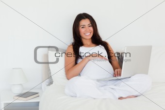 Pretty pregnant woman relaxing with her laptop while