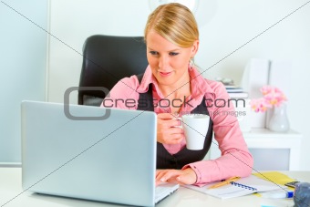 Happy business woman working on laptop and drinking coffee
