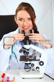 Smiling female medical doctor using microscope 
