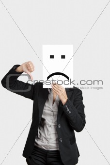 Woman showing a sad emoticon in front of face and making a thumbs down gesture with the right hand