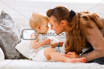 Cute baby with soother and young mom playing on divan
