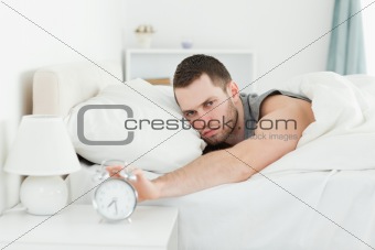 Tired young man switching off his alarm clock
