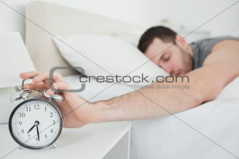 Sleeping young man being awakened by an alarm clock