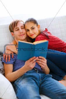 Romantic couple sitting on sofa and reading book
