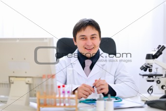 Smiling medical doctor sitting at table in office
