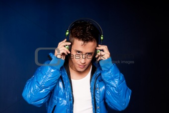 Young man listening music with headphones portrait on blue background