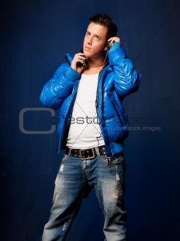 Young man listening music with headphones standing on blue background