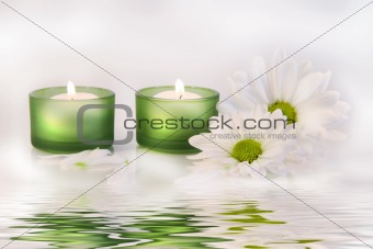 Green candles and daisies near water reflection