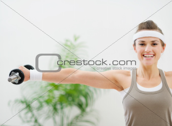 Smiling athletic woman making exercise with dumbbells