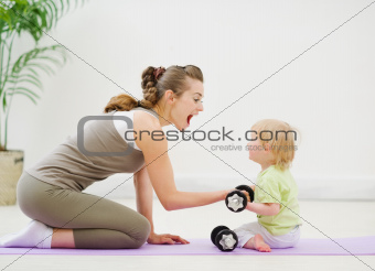 Baby helping mother lifting dumb-bells