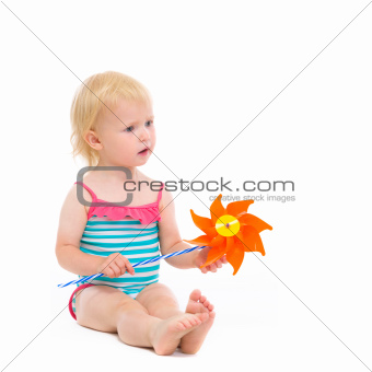 Thoughtful baby in swimsuit with pinwheel sitting on floor