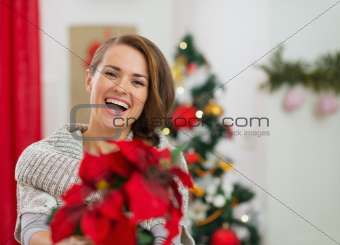 Smiling young woman holding Christmas rose near Christmas tree