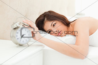 A woman lying on the bed with her hand on the alarm clock to sto