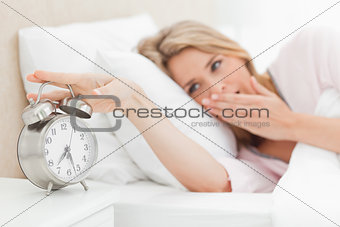 Woman waking up, yawning nd reaching over to silence alarm clock