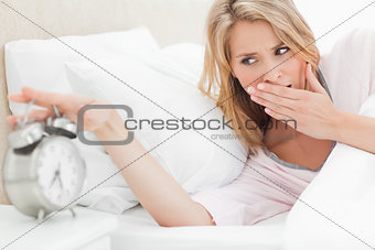 Woman reaching to silence alarm clock while glancing at the time