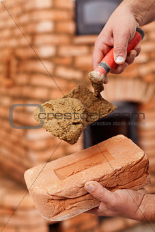 Masonry heater builder hand with brick and trowel