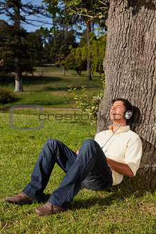 Man using headphones to sing along to music while resting a tree