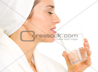 Young woman in bathrobe drinking water