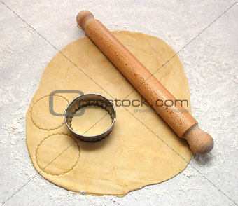 Rolling pin and cutter on fresh pastry, cutting out circles 