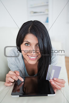 Woman smiling while holding a credit card and touching a tablet