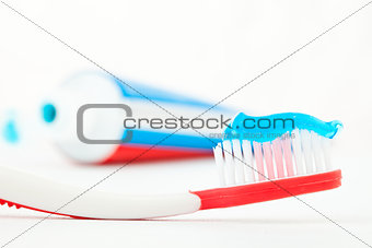 Tube of toothpaste next to a red toothbrush