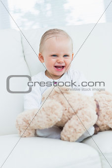 Baby smiling with teddy bear on his knees