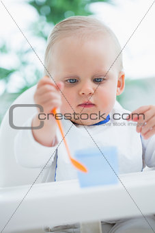 Baby looking at a plastic spoon while holding it