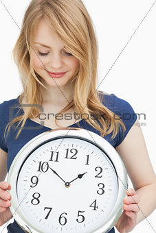 Blonde woman holding a clock while smiling
